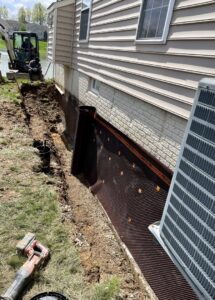 Exterior of house with trench and black drainage matting being installed by Pioneer Basement Solutions in Canton, OH.