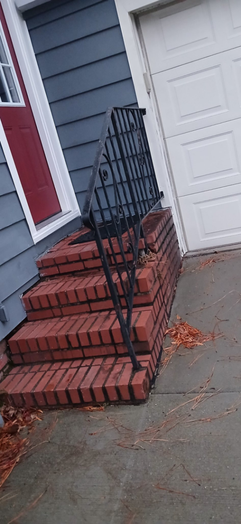 Exterior brick steps with a black metal railing leading to a house entrance, a handyman project by Coach Rose Painting Team in Norfolk, VA.