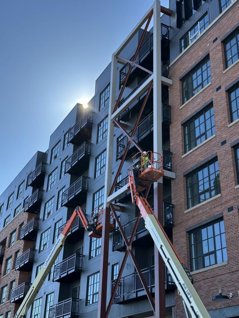 Workers on boom lifts performing exterior facade repair for Bell SPI - Shamrock Painting in Denver, CO.