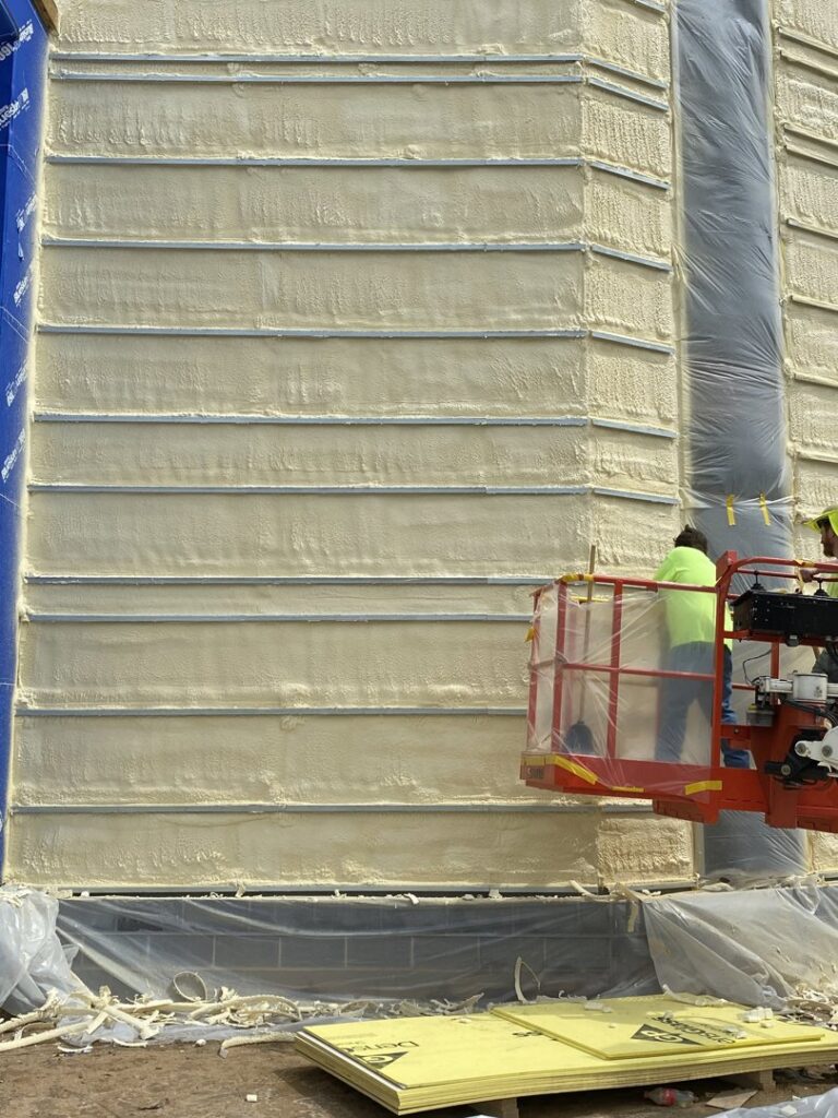 Workers in a boom lift applying spray foam insulation to the exterior of a large building under construction by Olympus Spray Foam in Philadelphia, PA.