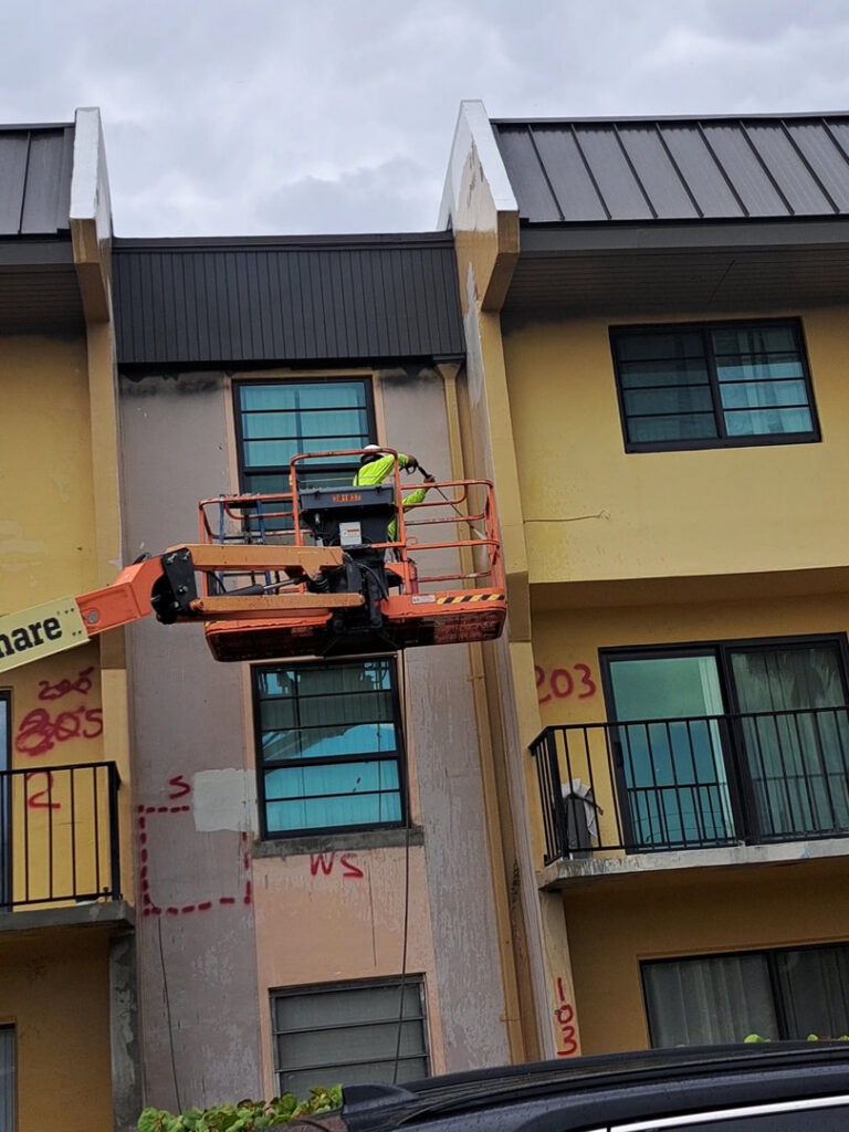 Worker in a boom lift performing exterior building maintenance for Vico Painting Contractors in Hialeah, FL