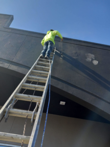 A worker performing exterior building maintenance on a tall ladder for Husky drywall LLC in Kansas City, MO.