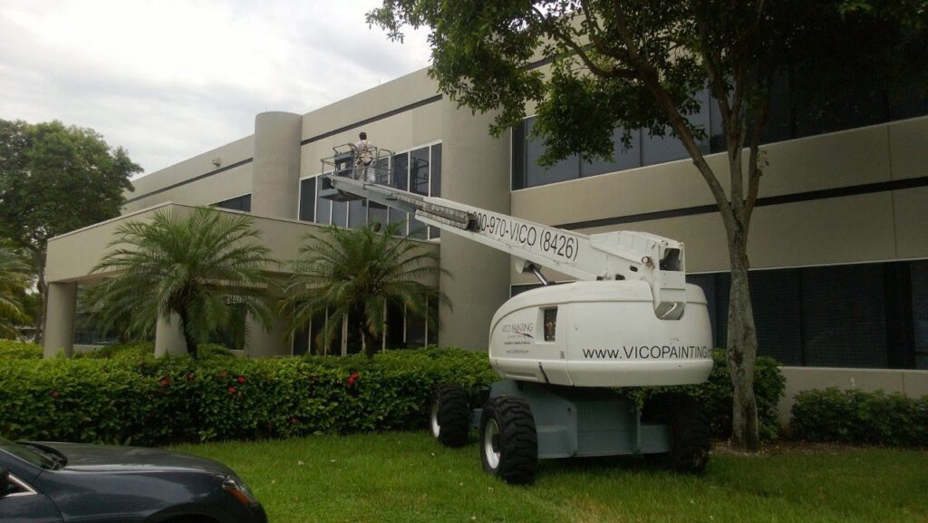 Worker in a boom lift performing exterior building painting for Vico Painting Contractors in Hialeah, FL