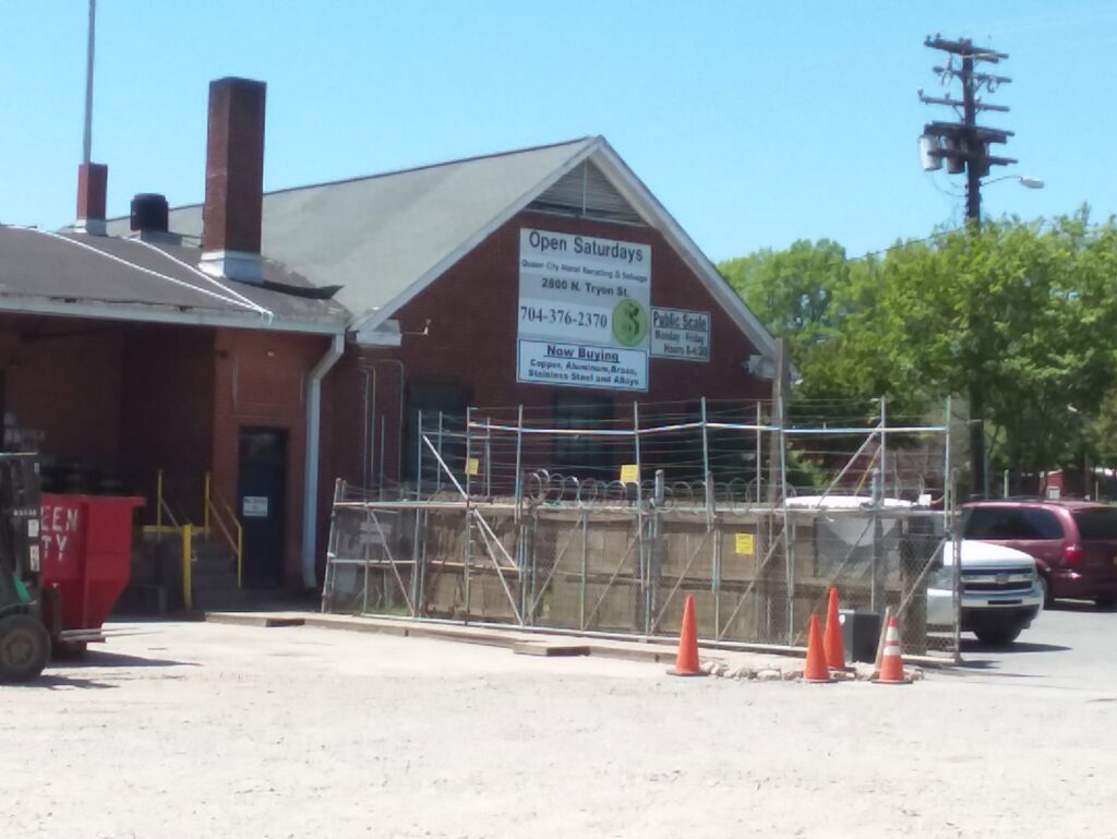 The exterior of Queen City Metal Recycling & Salvage building with signs indicating scrap buying services in Charlotte, NC.