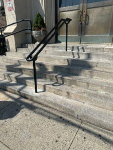 A black metal handrail installed on an exterior concrete staircase by Advanced Welding All in One Fabrication LLC in Guttenberg, NJ.