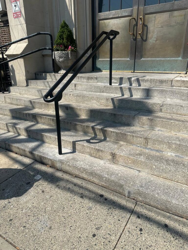 A black metal handrail installed on an exterior concrete staircase by Advanced Welding All in One Fabrication LLC in Guttenberg, NJ.