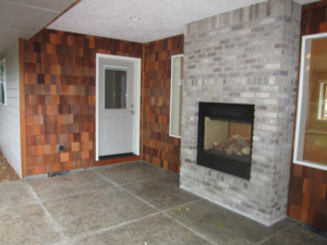 A covered patio with a brick fireplace, cedar shake wall, and an exterior door installed by Qual-i-Tee bilt homes - Steve Johnson in Salem, OR.