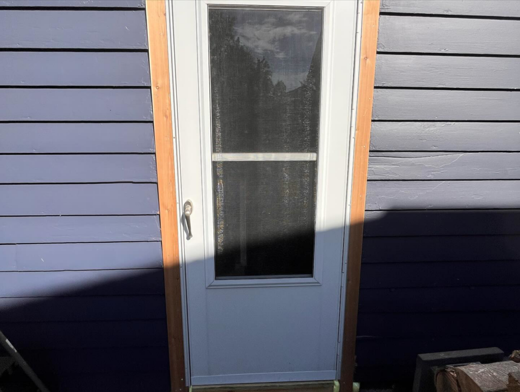 A newly installed exterior door with wood trim on a blue-sided house by McDonald Residential Contracting in Ames, IA.