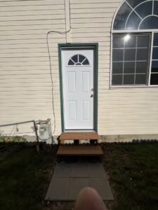 An exterior white door with green trim and newly installed wooden steps, completed by Forever Young Handyman Services in Boise, ID.