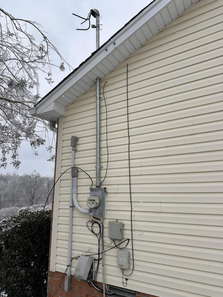 An exterior electrical meter and conduit system installed on a house with siding by HHS Contractors in Providence Village, TX.
