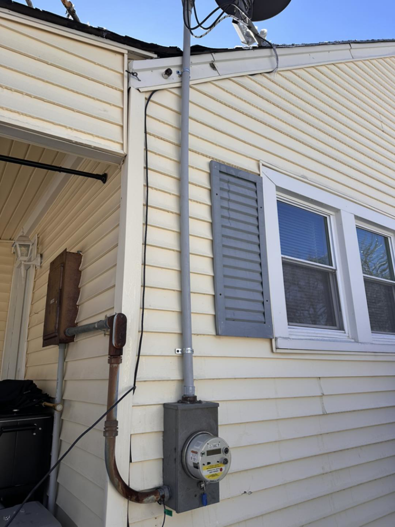 An exterior electrical meter and conduit system on a yellow-sided house by HHS Contractors in Providence Village, TX.