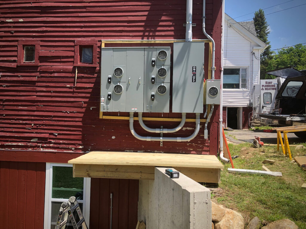 Multiple exterior electrical meters and conduits installed on the side of a red building by Paul Bergeron Jr. Contracting Inc. in Worcester, MA