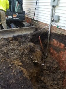 Exterior of house with large trench dug along foundation, showing exposed foundation for work by Pioneer Basement Solutions in Canton, OH.