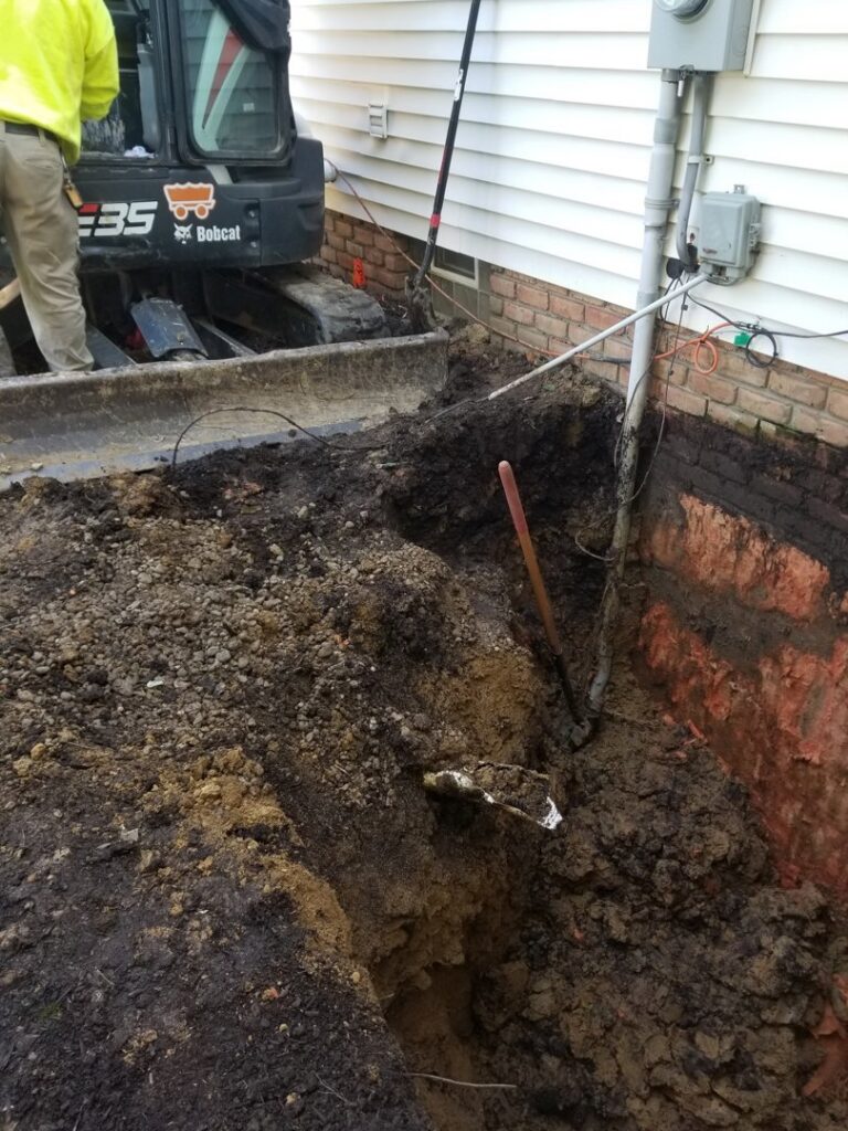 Exterior of house with large trench dug along foundation, showing exposed foundation for work by Pioneer Basement Solutions in Canton, OH.