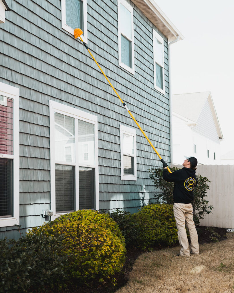 A worker performing exterior house cleaning with a long pole tool for Diamond Exterminators in Chesapeake, VA.