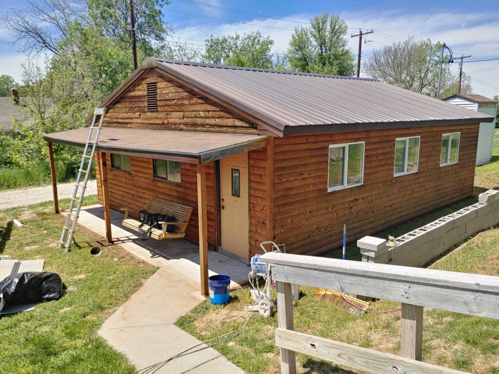 Exterior view of a cabin-style house with a ladder and painting equipment, indicating ongoing painting or maintenance work by Rapid Renovations LLC in Rapid City, SD.