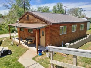 Exterior view of a cabin-style house with a ladder and painting equipment, indicating ongoing painting or maintenance work by Rapid Renovations LLC in Rapid City, SD.
