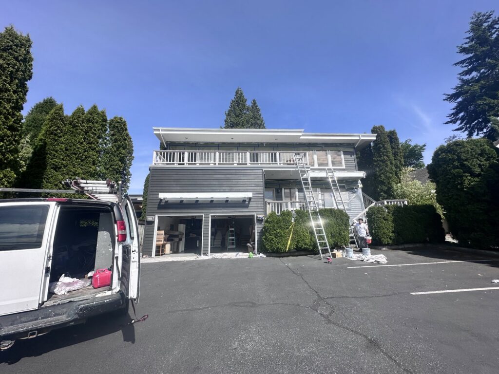 Exterior house painting in progress with multiple ladders and a work van by J&R Buezo Painting Services LLC in Everett, WA