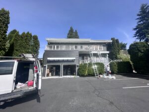 Exterior house painting in progress with multiple ladders and a work van by J&R Buezo Painting Services LLC in Everett, WA
