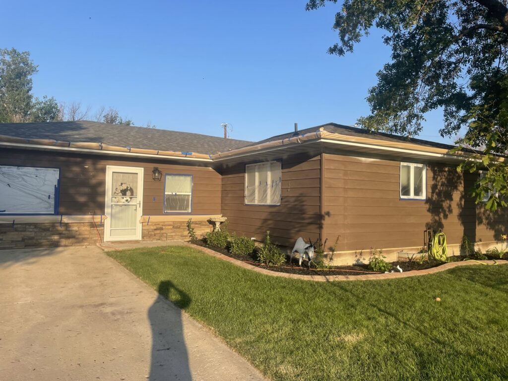 The exterior of a house with brown siding, windows taped off for painting or siding work, by Knutson's Property Maintenance Llc in Williston, ND.