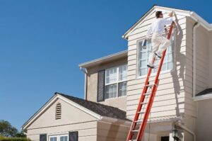A professional painter on a ladder applying fresh paint to the exterior of a house by Total Improvements LLC in San Antonio, TX