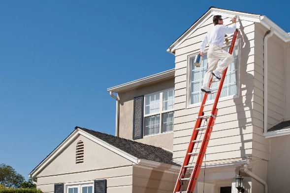 A professional painter on a ladder applying fresh paint to the exterior of a house by Total Improvements LLC in San Antonio, TX