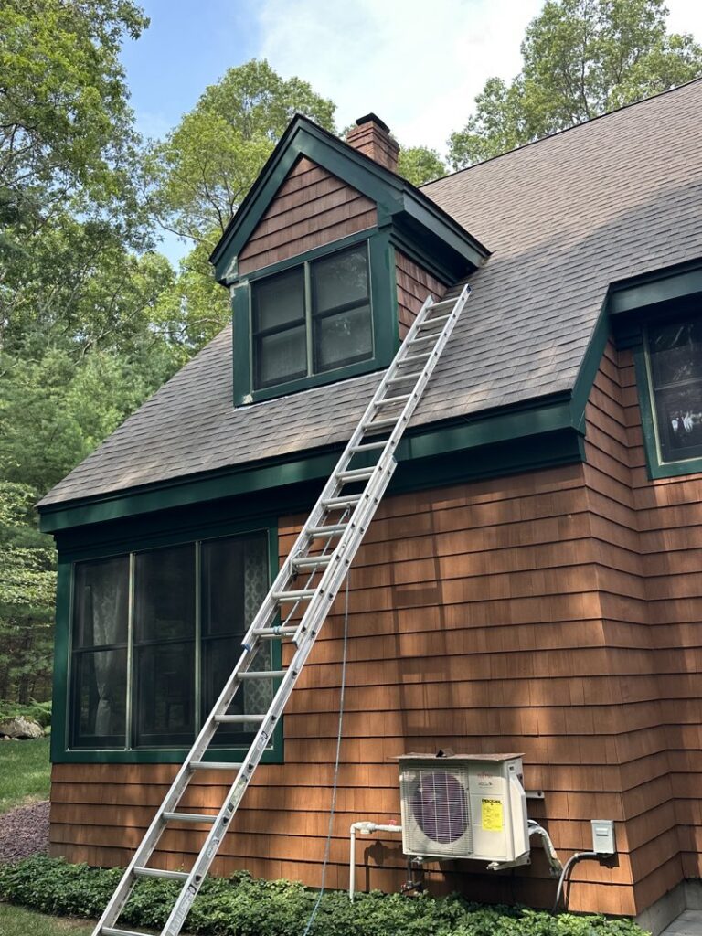 A ladder leaning against a house with cedar shingles, indicating exterior repair work by Woodbine Repair & Remodeling in Jamestown, RI.