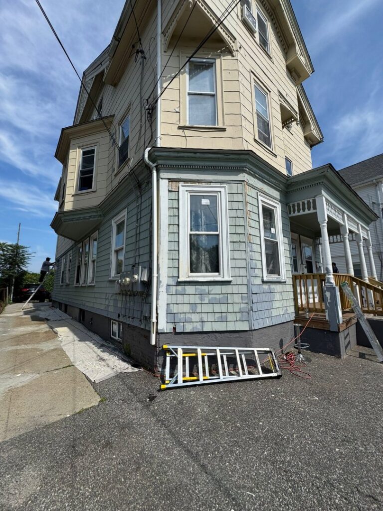The exterior of a house with a ladder, showing siding work and painting in progress by Quinonez Painting & Renovations LLC in Providence, RI.