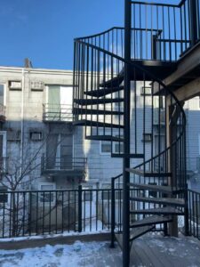 A custom-fabricated black metal exterior spiral staircase leading to an upper deck, installed by Advanced Welding All in One Fabrication LLC in Guttenberg, NJ.