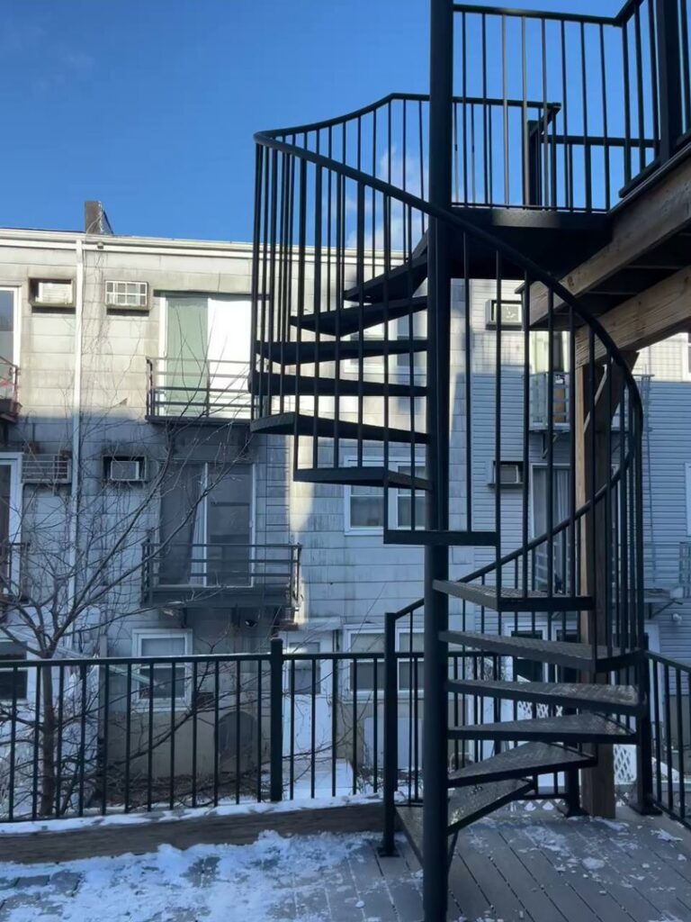 A custom-fabricated black metal exterior spiral staircase leading to an upper deck, installed by Advanced Welding All in One Fabrication LLC in Guttenberg, NJ.