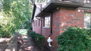 An exterior dark brown radon mitigation system installed on a brick house by All Ohio Radon Services in Akron, OH.
