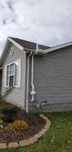 A white radon mitigation system installed on the exterior of a gray house by All Ohio Radon Services in Akron, OH.