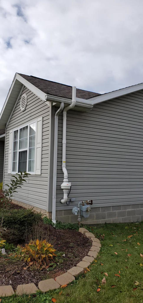 A white radon mitigation system installed on the exterior of a gray house by All Ohio Radon Services in Akron, OH.