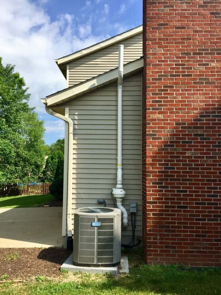An exterior white radon mitigation system installed next to an AC unit on a house by All Ohio Radon Services in Akron, OH.