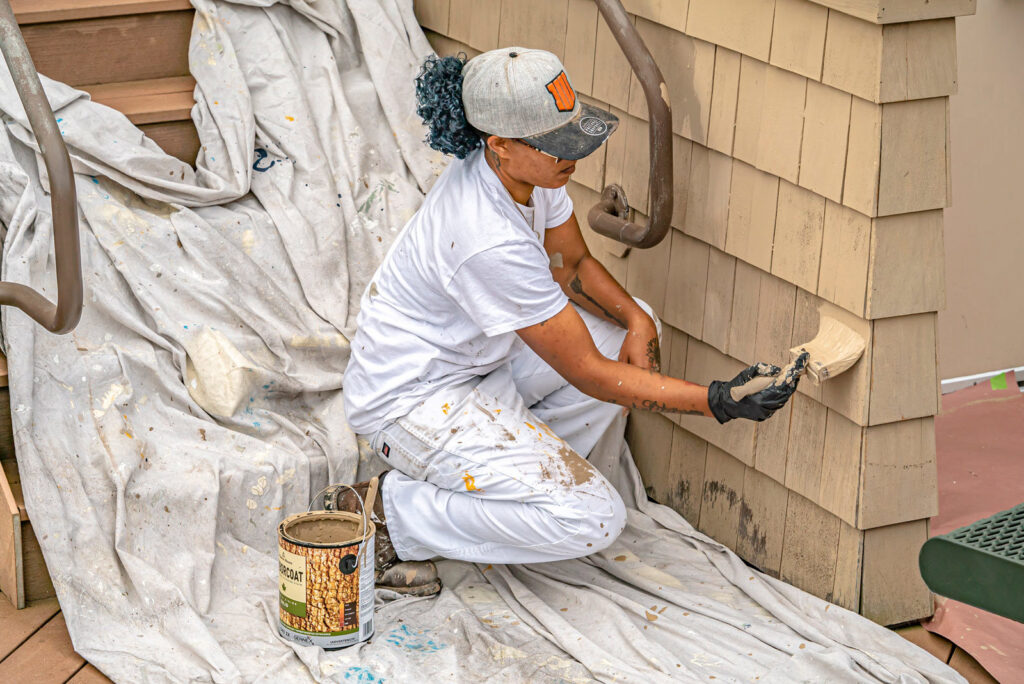 A professional painter from GO Painting applying paint to exterior siding with a brush in New Haven, CT