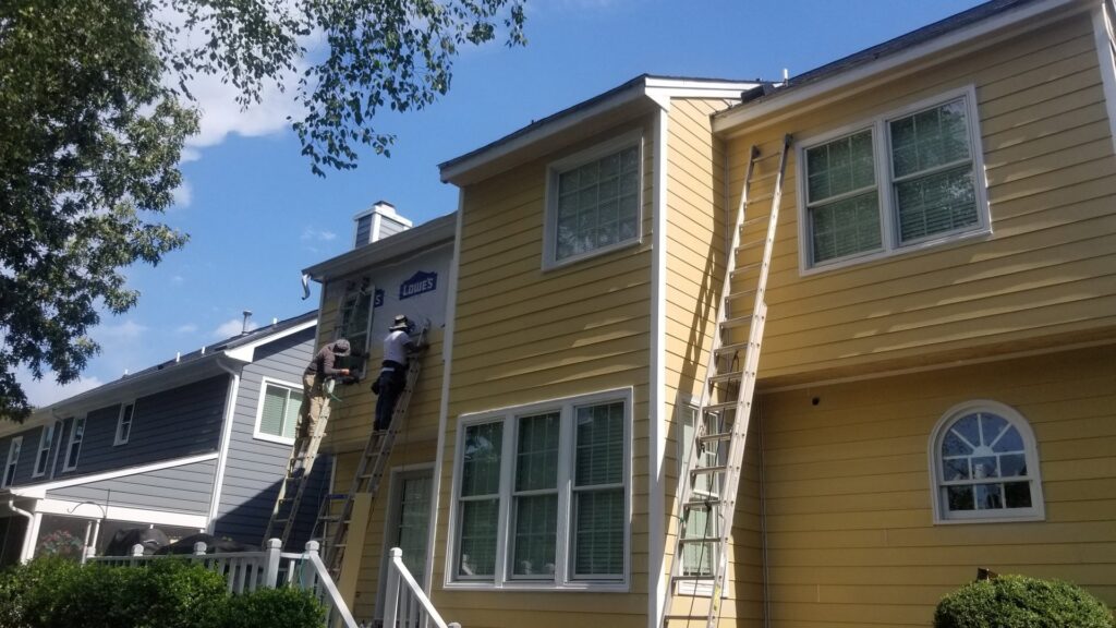 Workers on ladders performing exterior siding repair or installation on a house for Albis Morales Painting LLC in Raleigh, NC.