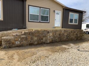An exterior view of a house featuring a newly constructed stone retaining wall and steps by Brewer Builds in Fort Worth, TX.