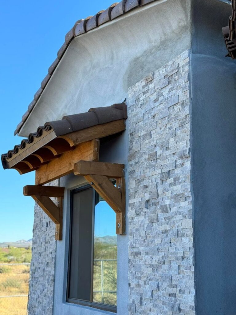 Close-up of a house exterior under construction, showing stone veneer and a wooden awning installation by Kelso Custom Builders, Inc. in Phoenix, AZ.