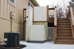 An exterior vertical platform lift installed next to a wooden deck by Thrive Homes, LLC in Olathe, KS.