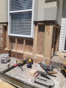 An exterior wall undergoing repair with exposed wood framing and various tools on a workbench by Modern Wall Systems in Virginia Beach, VA.