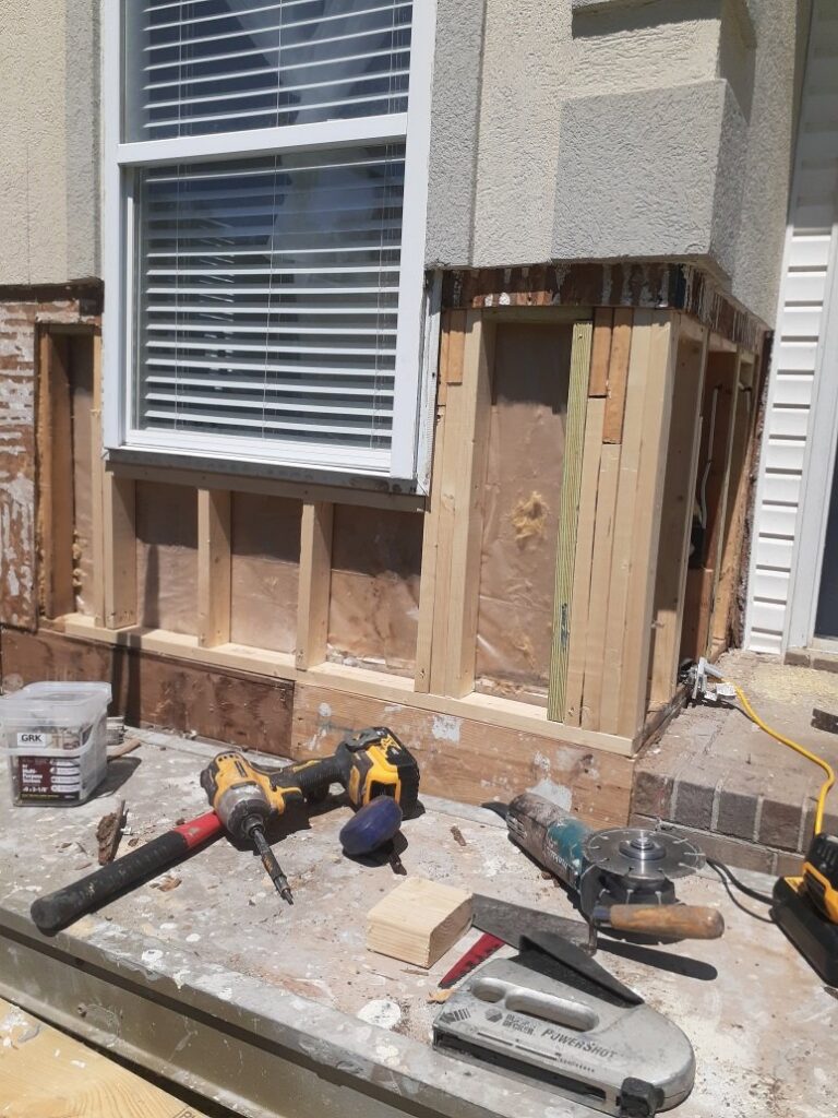 An exterior wall undergoing repair with exposed wood framing and various tools on a workbench by Modern Wall Systems in Virginia Beach, VA.