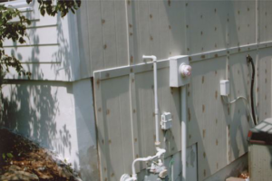 An exterior wall with visible wood grain, pipes, and electrical components, showing work in progress by AAA Lifetime Exterior & Remodeling LLC, Kansas City, MO.
