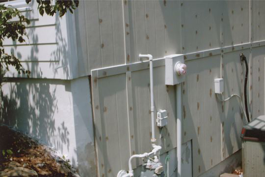 An exterior wall with visible wood grain, pipes, and electrical components, showing work in progress by AAA Lifetime Exterior & Remodeling LLC, Kansas City, MO.