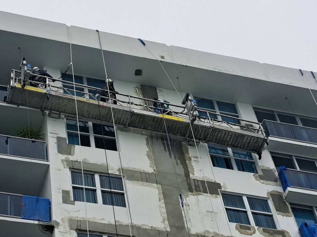Facade repair and surface preparation by workers on a suspended scaffold for Vico Painting Contractors in Hialeah, FL