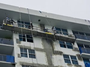 Facade repair and surface preparation by workers on a suspended scaffold for Vico Painting Contractors in Hialeah, FL