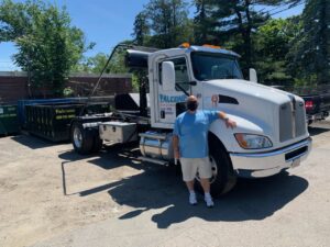 An employee of Falcone Enterprises stands proudly in front of a junk removal truck with a dumpster in Worcester, MA.