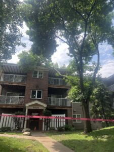 A tree branch fallen on an apartment building, marked with danger tape, indicating emergency tree service by JN Services LLC in Des Moines, IA.