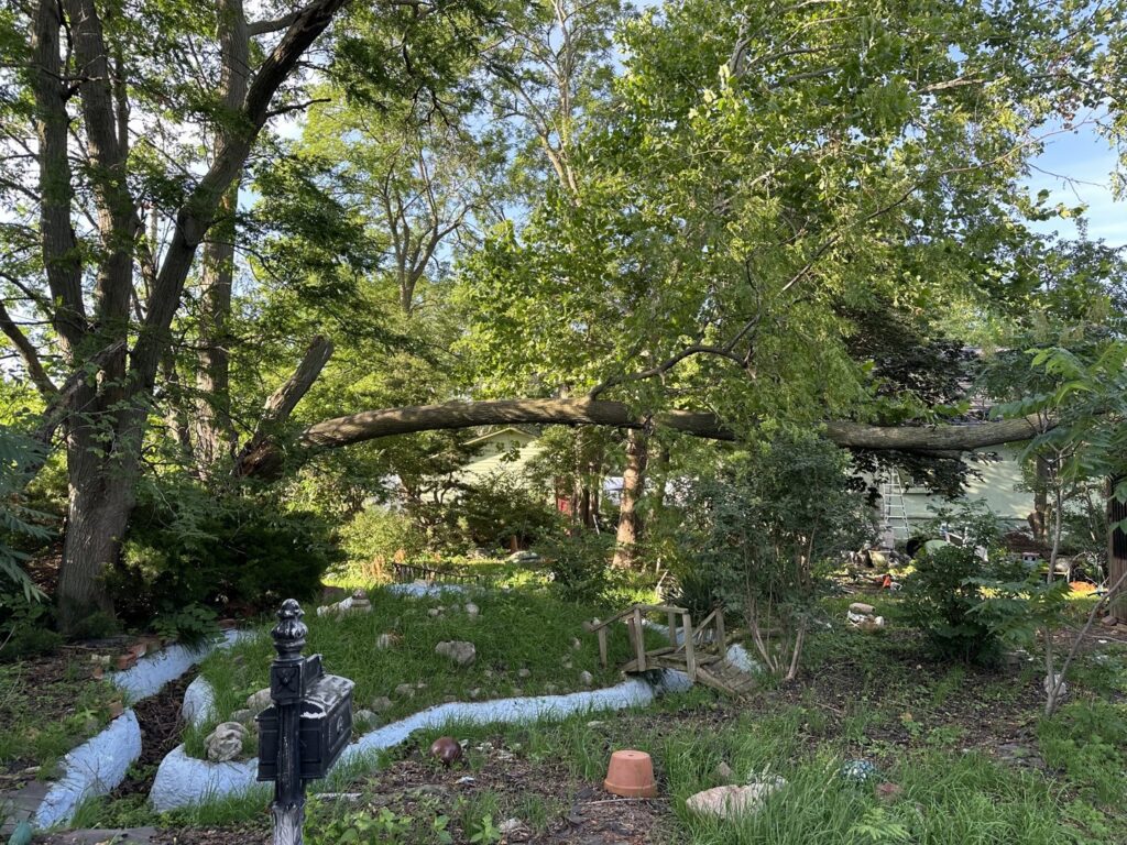 A large fallen tree branch resting precariously over a house, requiring emergency tree service from JOCO Services LLC in Council Bluffs, IA.