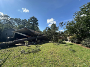 A large fallen tree lying across a damaged house, indicating storm damage cleanup services by GNC Tree Service, LLC in Columbia, SC.