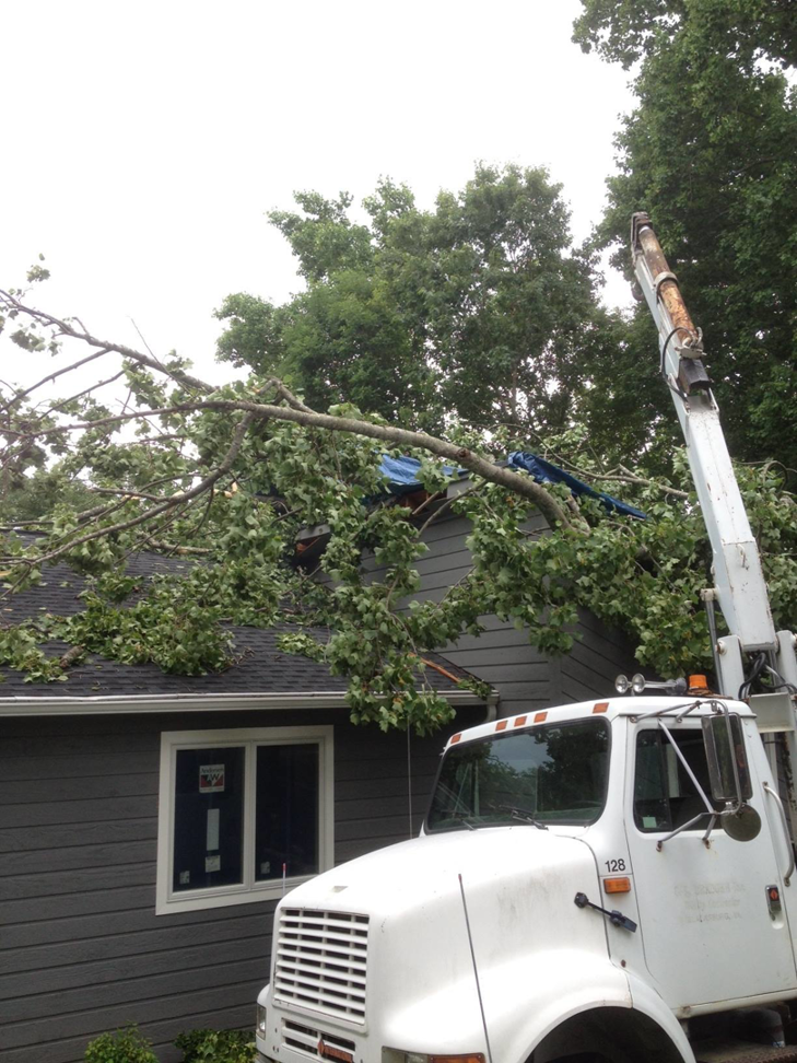 A crane truck prepares to remove a fallen tree and branches from a residential roof, performed by Mark's Tree & Stump Removal in Roanoke, VA.